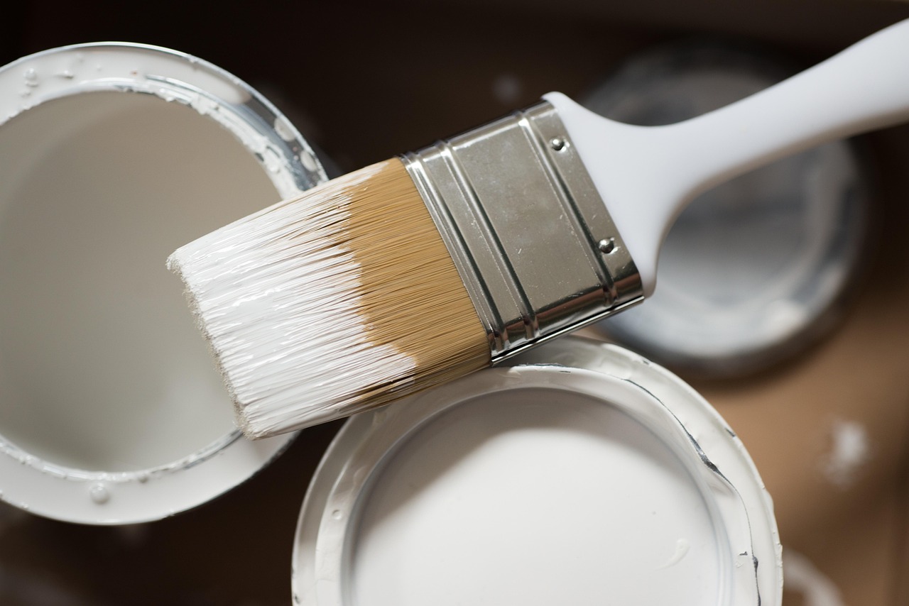 Two paint tins with white paint inside and a paintbrush positioned in the middle